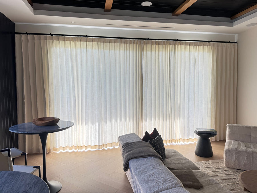 Full-width sheer drapery under a dark beamed ceiling in a living room