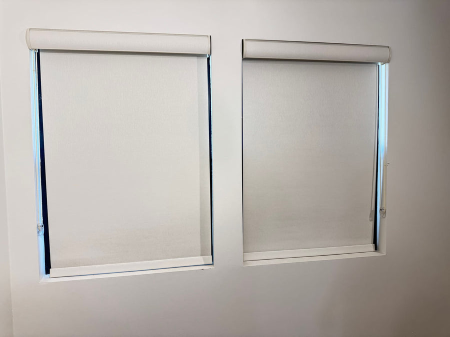Pair of roller shades mounted inside matching window recesses on a white wall