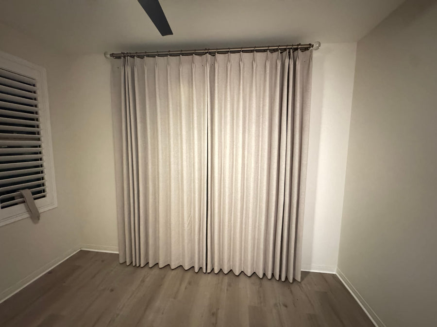 Floor-length oatmeal drapery panels on a metal rod beside a shuttered window