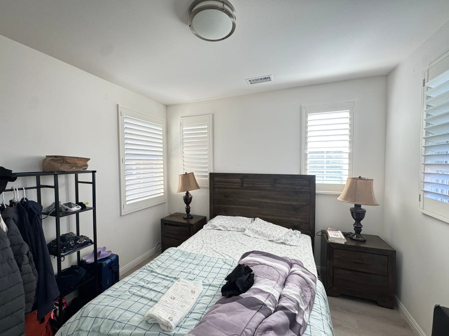 Corner bedroom windows with shutters framing soft daylight