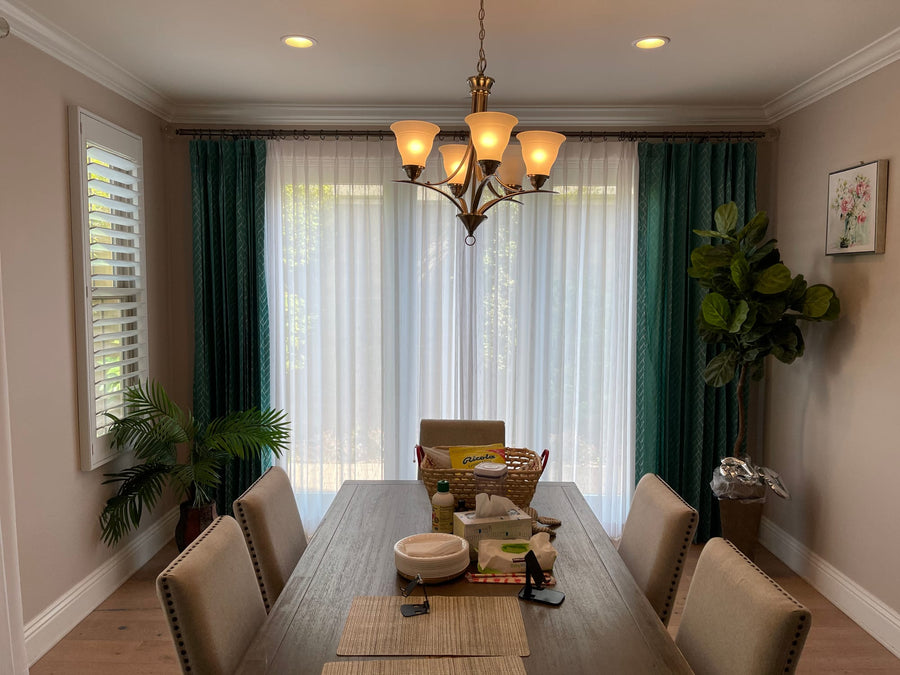 Sheer pinch-pleat panels framed by patterned teal drapery