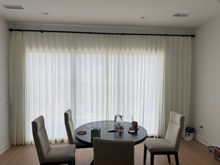 Dining area with floor-length sheer panels filtering daylight behind a round table