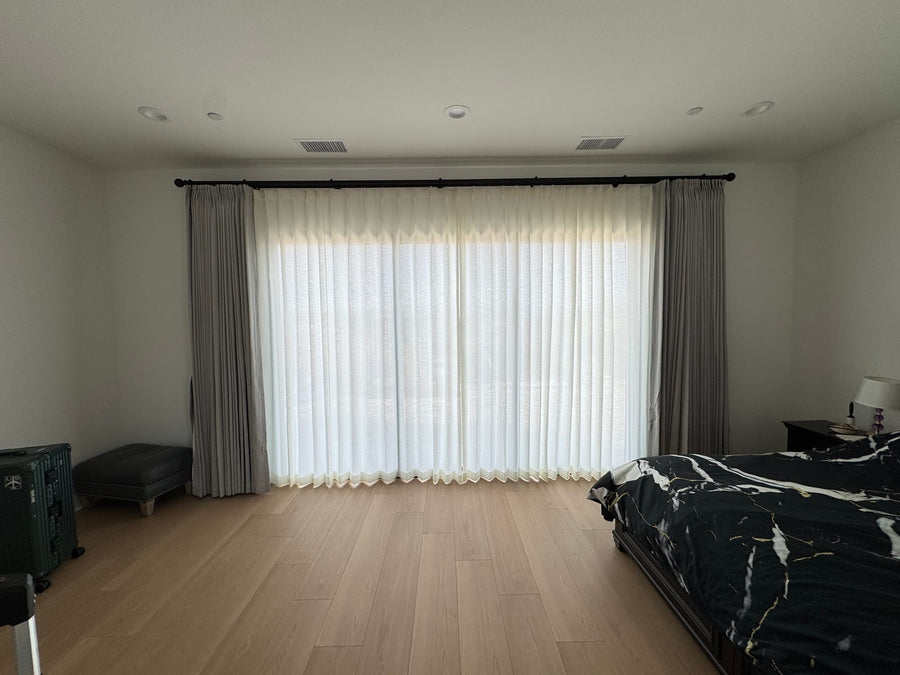 Bedroom window layered with ivory sheers and grey side drapery panels