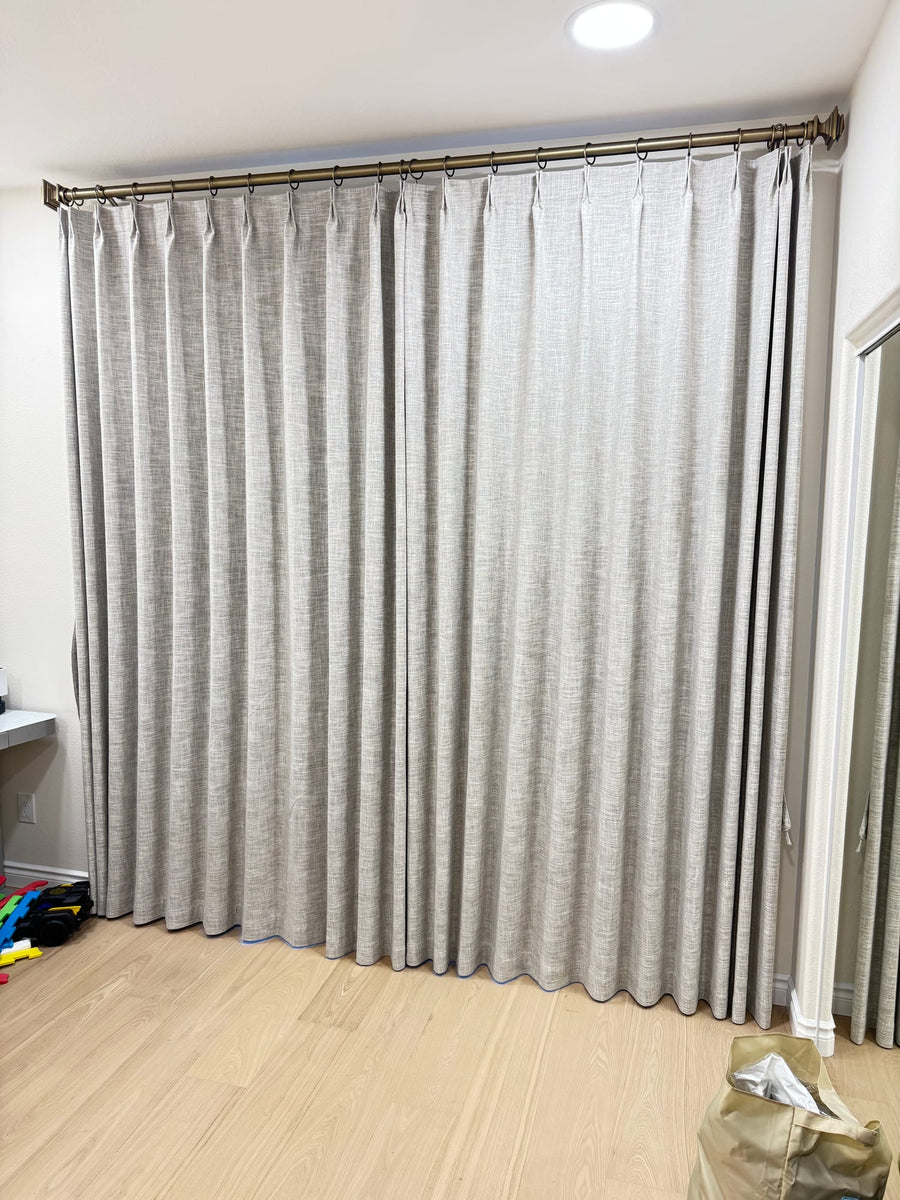 Pinch-pleat textured drapery on a brass rod covering a full wall of glass