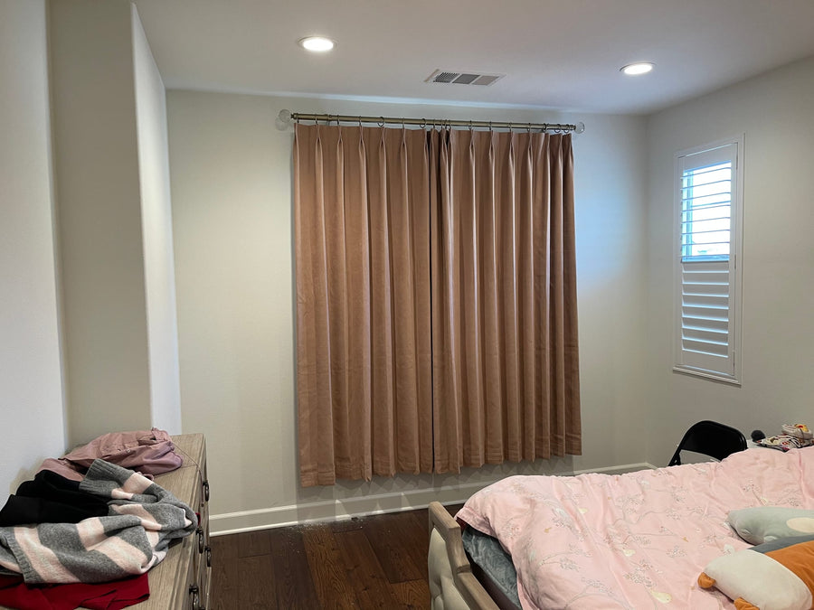 Camel drapery panels beside a shuttered side window in a bedroom