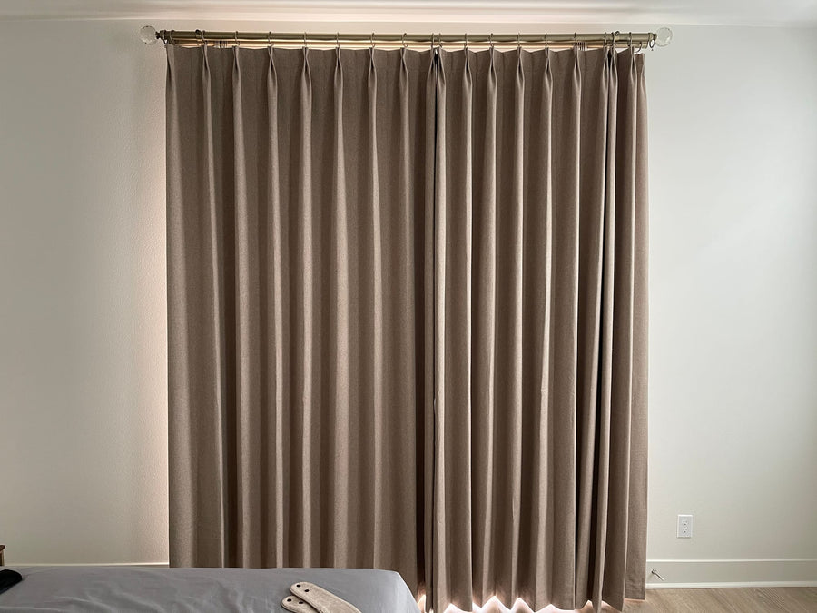 Closed taupe drapery panels in even folds against a pale wall and light wood floor