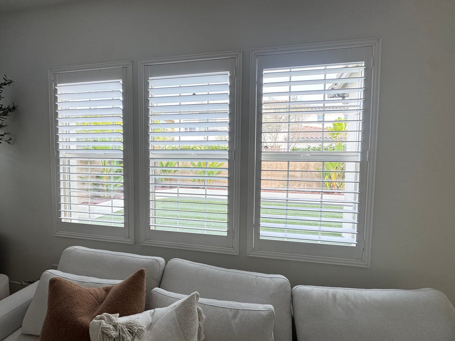 Bank of three shuttered windows above a pale sectional sofa
