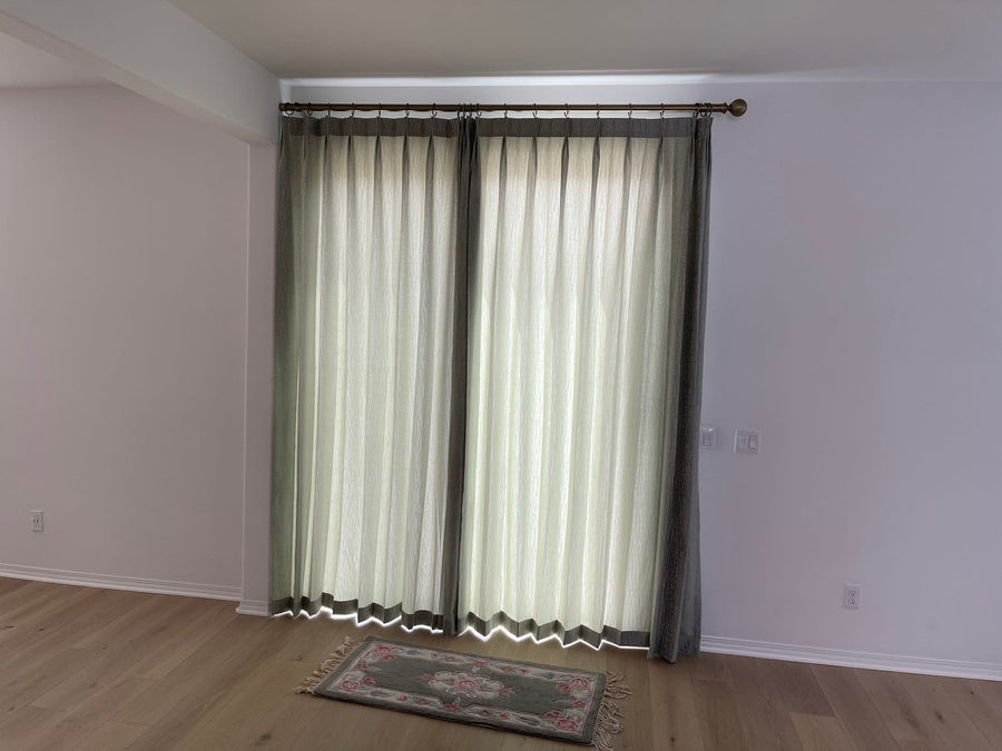 Layered sheer and drapery on a shared brass rod with banded edges